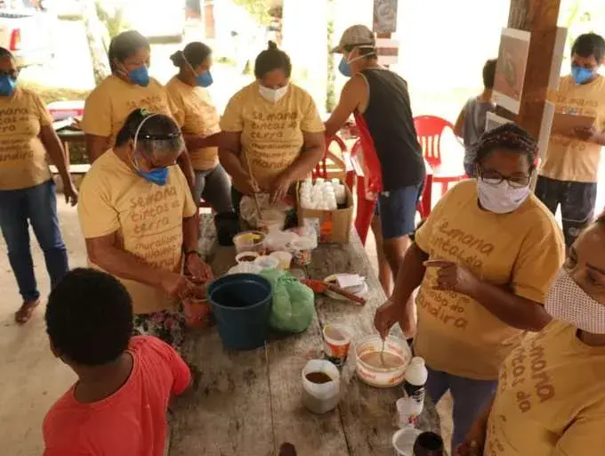 Moradores do Quilombo do Mandira reunidos ao redor de uma mesa preparando tintas de terra