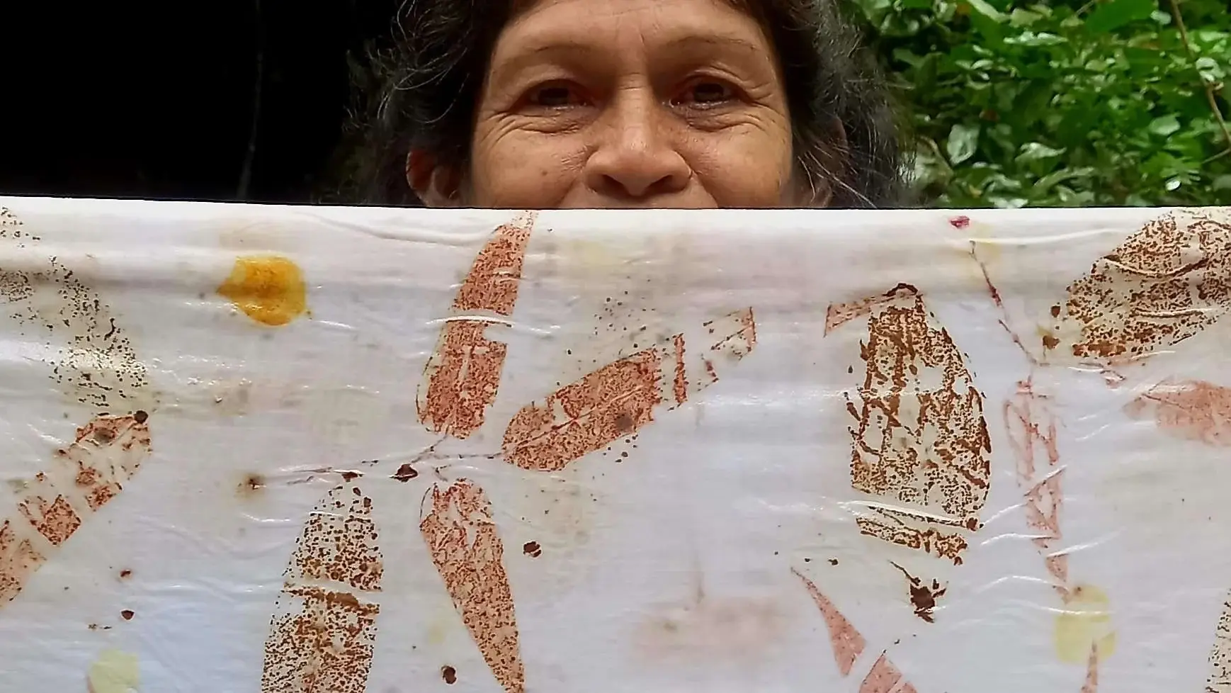 Ilda Poty segurando um tecido com impressão botânica em tons de ferrugem, amarelo e rosa